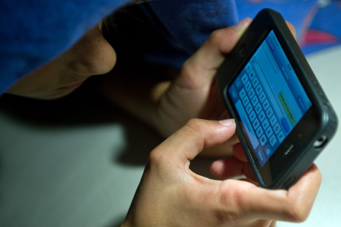 Ein elfjähriger Junge liegt unter der Bettdecke und schreibt auf einem Smartphone eine SMS. Kinder unter 13 Jahren sollten Experten zufolge keinen Zugang zu derartigen Medien haben.